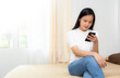 © BrightSpace - Young casual beautiful asia woman sit relax on bed in bed room surfing wireless internet on smartphone at home, message text on modern cellphone, shopping online via website, copy space