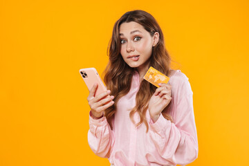 Poster - Image of nice confused woman holding credit card and mobile phone