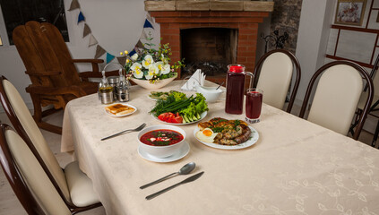 Russian lunch with red borsch, fried egg, fried sausage, bacon and potato pancakes. Closeup photo of Russian hot main meal. Loft interior of dining room. Brick fireplace, rough wooden arm-chair.