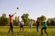Happy friends playing volleyball game in countryside on summer day. Group of students having fun together outdoors
