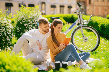 Woman with tablet and man sitting on grass on picnic