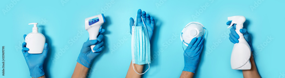 Raised hands in medical gloves holding masks, sanitizers, soap, non contact thermometer on blue background. Banner. Copy space. Health protection equipment during quarantine Coronavirus pandemic - obrazy, fototapety, plakaty 