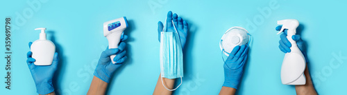 Fotomural Raised hands in medical gloves holding masks, sanitizers, soap, non contact thermometer on blue background