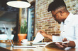 © BullRun - Concentrated afro american male finance advisor checking documentation and accounting reports of company income to create successful strategy for increasing sales working in cafe using gadgets