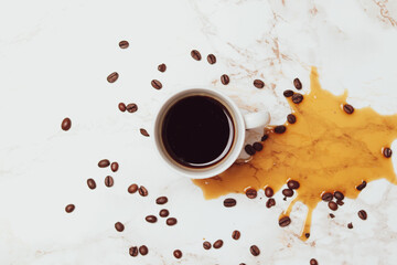 white coffee cup filled with coffee, coffee beans an a coffee stain on marble background, top view