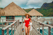 beautiful girl in red swimsuit posing on dock near tropical houses on water