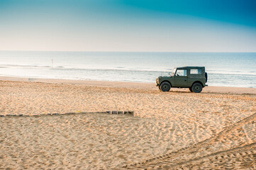 Vintage jeep parked on a deserted beach at sunrise in summer time , clear sky with no clouds , holiday scene