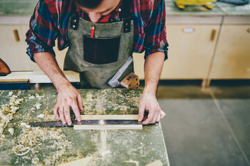 Wall Mural - cropped image of strong male carpenter in apron checking measures of wooden brick making constructio
