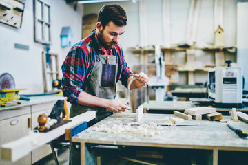 Wall Mural - serious bearded male joiner making details by himself using sharp tools for timber on working space,