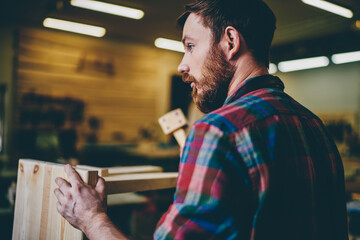 Wall Mural - handsome bearded craftsman working with hammer repair furniture in workshop, rear view of caucasian 
