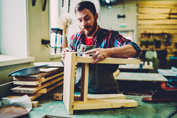 Wall Mural - bearded woodworker in apron concentrated in garage repairing chair using tools equipment indoors, ha