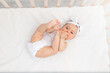 © Any Grant - baby girl 6 months old lies in a crib in the nursery with white clothes on her back and laughs, looks at the camera, baby's morning, baby products concept