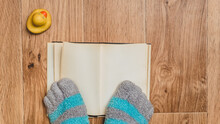 Striped Socks With Toes Against A Background Of A Book, A Wooden Floor, And A Rubber Duck. Comfortable Clothing For The Legs At The Weekend.