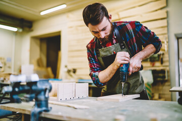 Wall Mural - young professional male carpenter drilling wooden plank for creating own decorative construction con