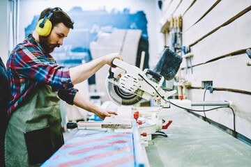 Wall Mural - professional male carpenter in equipment for safety and protection concentrated on making wooden pla