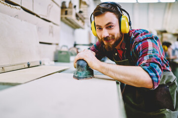 Wall Mural - cheerful caucasian male in protective equipment making polish with sander satisfied with his occupat