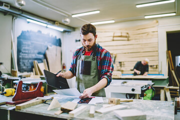 Wall Mural - serious caucasian male owner of carpentry business checking notes from clients orders standing near 