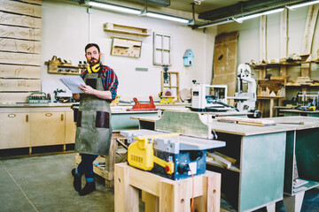 Wall Mural - pensive male engineer in apron holding paper for making sketch and planning working in own workshop 