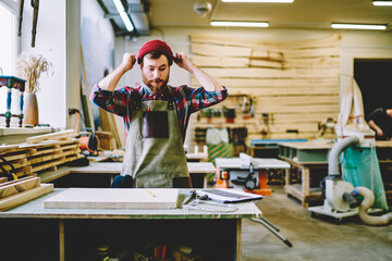 Wall Mural - emotional hipster guy in apron disappointed with failure during carpentry courses gesture raising up