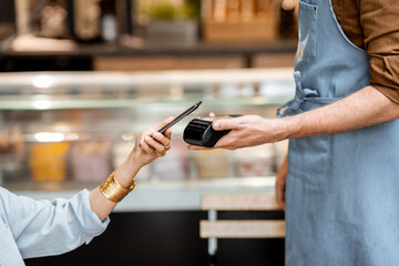 Female client paying by phone contactlessly at the cafe, close-up