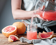 Woman Pouring Pink Grapefruit Juice From Glass Jug Into A Cocktail Glass