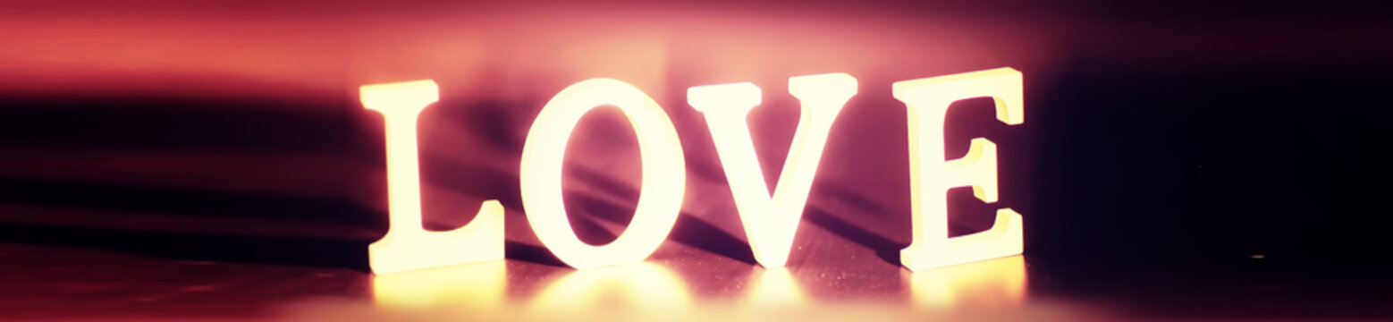 Wooden and metal letters forming word LOVE written on dark black background with lights.