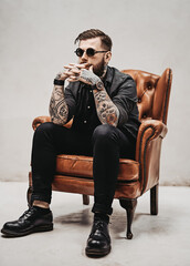 Wall Mural - Bearded tattooed man sits on a vintage chair with a thoughtful look