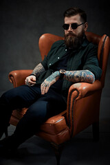 Wall Mural - Cool bearded young man sitting on a vintage chair in a dark studio