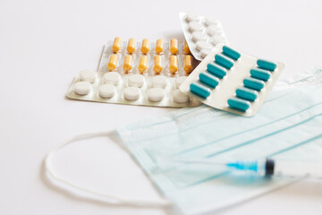 portion of pills on the background of a three-layer medical mask with rubber ear straps, a syringe and various medicines, tablets.The concept of medicine