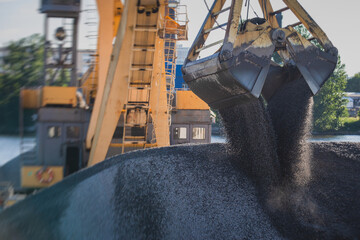 Bulk-handling crane unloading sand, road metal and gravel from cargo vessel ship, heavy vehicle and portal crane loader working with bulk materials in dock terminal