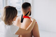 © dsheremeta - Physiotherapist applying red and black kinesio tapes to patients back in his office. Close up
