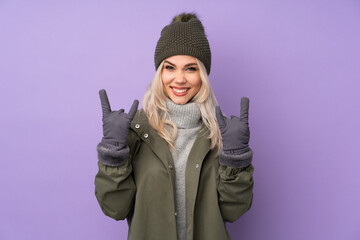 Teenager blonde girl with winter hat over isolated purple background making rock gesture