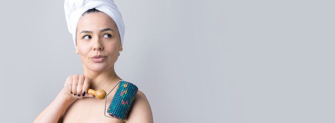 Brunette with a towel on her head using roller for face massage isolated on grey background