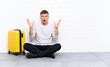 © luismolinero - Young handsome man sitting on the floor with a suitcase with surprise facial expression