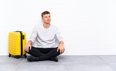 Young handsome man sitting on the floor with a suitcase laughing and looking up