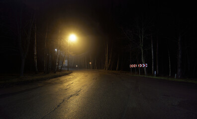 Wall Mural - An empty motorway with a sharp turn in a fog at night. Road sign close-up. Dark urban scene, cityscape. Riga, Latvia. Dangerous driving, speed, freedom, concept image