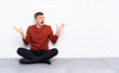 © luismolinero - Young handsome man sitting on the floor with surprise facial expression