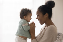 Happy Young African American Mother And Cute Little Girl Enjoying Tender Moment Profile Portrait, Loving Caring Mum Holding Pretty Toddler Infant Hands, Looking In Eyes, Childcare Concept