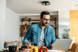 © bnenin - Handsome man at kitchen table using laptop, looking for a cooking recipe.