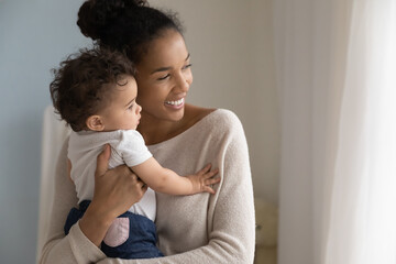 smiling dreamy african american young mother holding cute little daughter close up, looking to aside