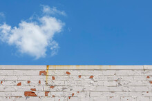 Top Of An Orange Brick Wall With Peeling White Paint Under A Blue Sky With Clouds