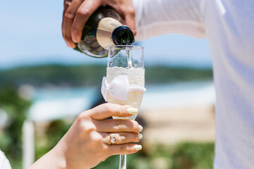 Champagne sparkling wine bottle and glasses at outdoors wedding catering event pouring into the glass and holding hand.Party and celebration.