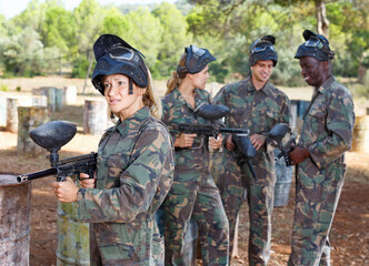 Wall Mural - Young woman wearing uniform and holding gun ready for playing paintball with friends outdoor