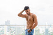 Young handsome muscular Persian man shirtless and looking down against view the city