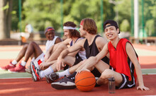 Smiling Asian Basketball Player With His Diverse Team Sitting On Outdoor Game Court, Copy Space