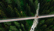 Aerial view of rope walkway through treetops in coniferous forest. Bird's eye view of hanging bridge crossing raging mountains river, suspension bridge with walking people traveller