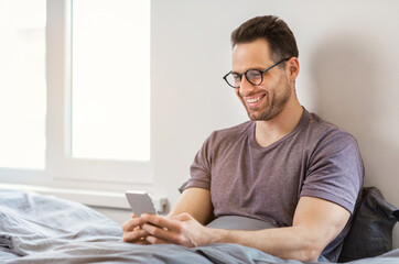 Aufkleber - Smiling Man Using Smartphone App Sitting In Bed At Home