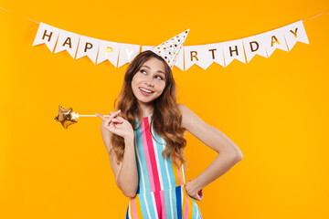 Wall Mural - Image of pleased cute woman in party cone posing with magic wand