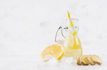 Summer homemade drink - infused lemon water with ice cubes, ginger, slices, soda, straw in yoke bottle in soft light white interior, copy space.