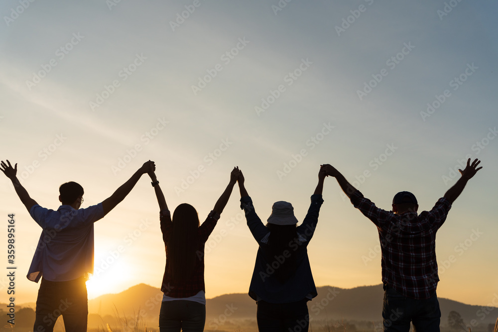 Group of happy friends are having fun with raised arms together in front of mountain and enjoy sunrise sunset showing unity and teamwork. Friendship happiness leisure partnership team concept. - obrazy, fototapety, plakaty 